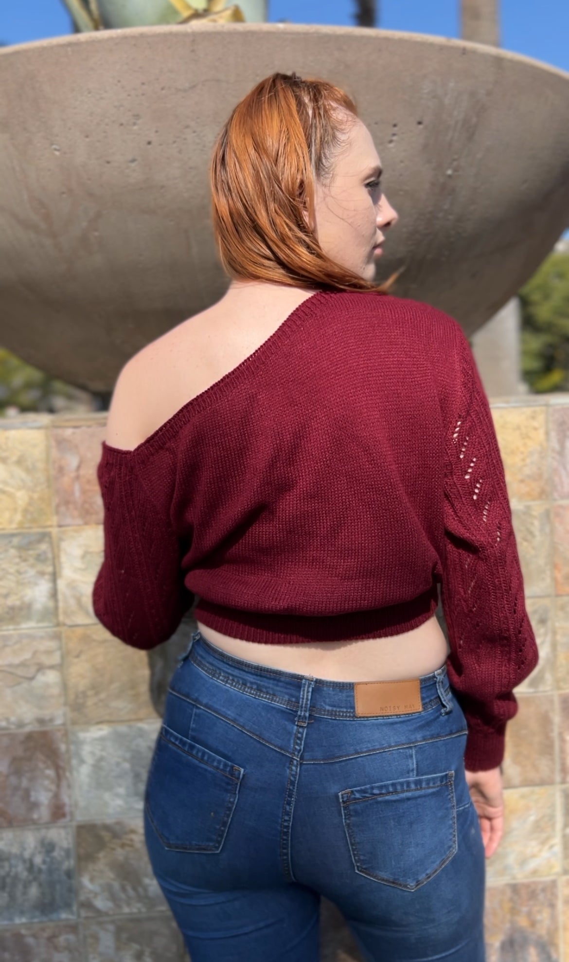 Woman in Burgundy One Shoulder Sweater facing backwards up close